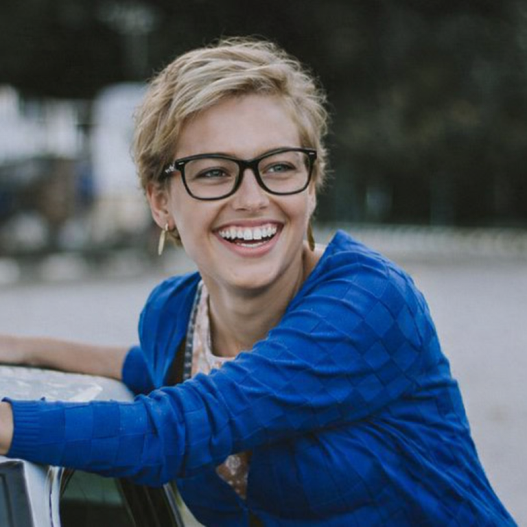 Femme souriante portant des lunettes de vue, vision confortable au quotidien, accompagnée par un opticien à Boulazac près de Périgueux Femme souriante aux cheveux courts et aux lunettes, portant un pull bleu.